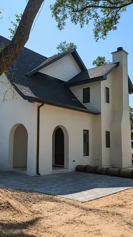 Black downspout on a white two-storey home with a dark shingle roof and arched porch, during construction