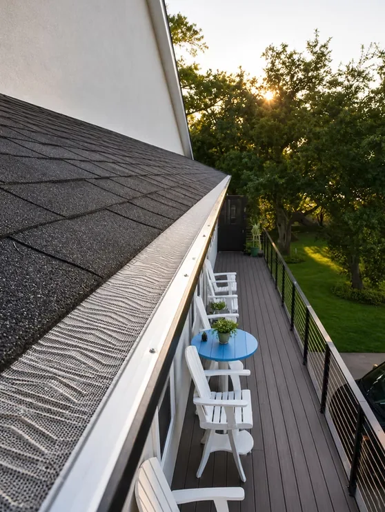 Micro-mesh gutter guard fitted along a dark shingle roof edge, looking down over a composite deck with white chairs