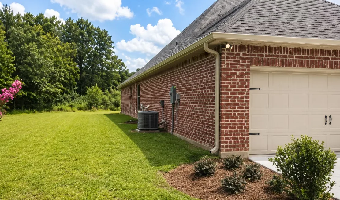 Cream gutter and downspout along the side of a red brick single-storey home, beside the garage and air-conditioning unit